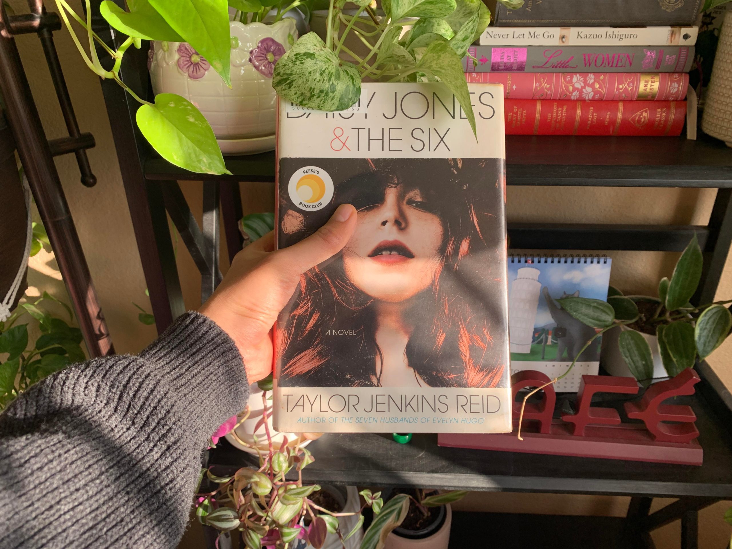 Hand holding copy of Daisy Jones and The Six next to plants